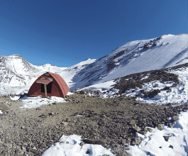 Una tienda de campaña roja se encuentra en la cima de una montaña nevada cubierta de plomo.