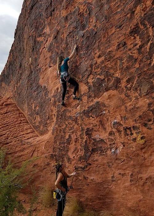 Dos personas usando cuerda para escalar una roca roja en el desierto.