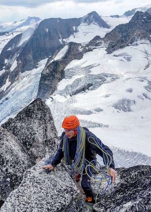 Un hombre ascendiendo una montaña con un glaciar al fondo.