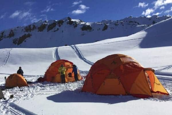 Un grupo de tiendas de campaña rando instaladas en la nieve de una montaña.