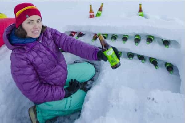 Una mujer rando sentada en la nieve con una botella de cerveza.
