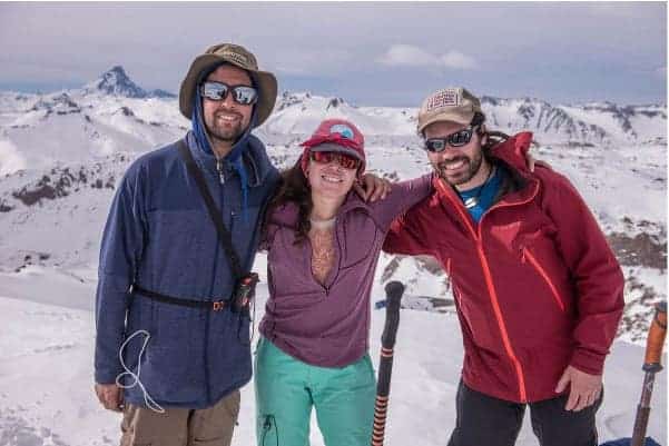 Tres personas rando posando para una foto en una montaña nevada.