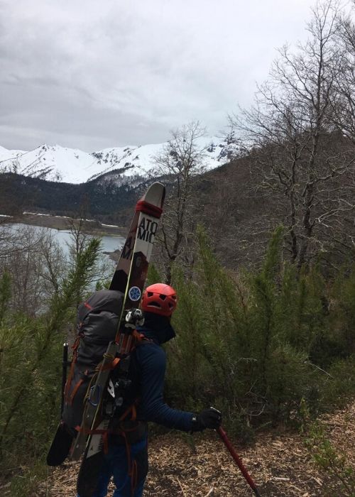 Una persona cargando esquís por un sendero con montañas al fondo, rodeado por la majestuosa presencia de un volcán.