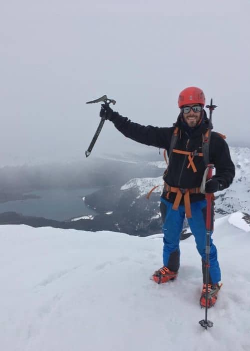 Un hombre parado en la cima de una montaña cubierta de nieve, con vistas a un majestuoso volcán.