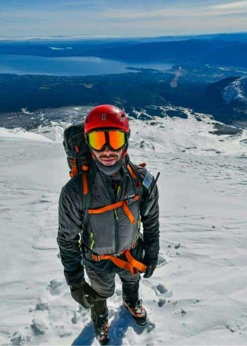 Un hombre con casco y gafas parado en la cima de una montaña nevada.