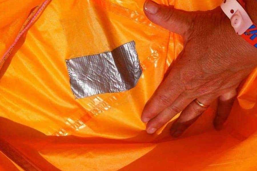 La mano de una persona sostiene un trozo de papel de aluminio dentro de una bolsa naranja asegurada con cinta adhesiva.