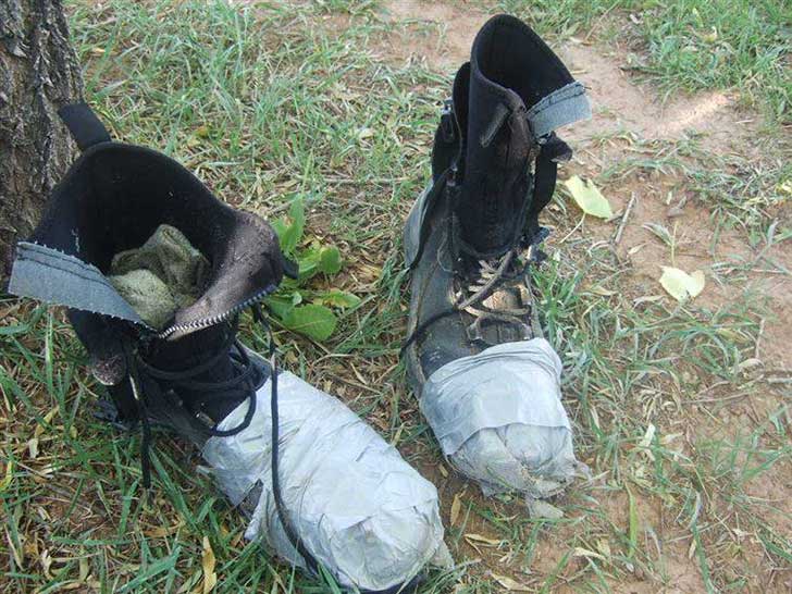 Un par de botas aseguradas con cinta adhesiva cubiertas con una envoltura de plástico en el suelo.