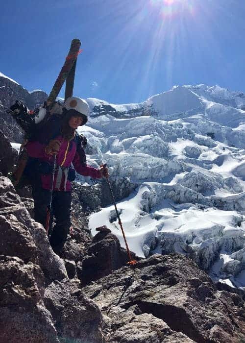 Una mujer ascendiendo a mayores altitudes en una montaña con sus esquís.