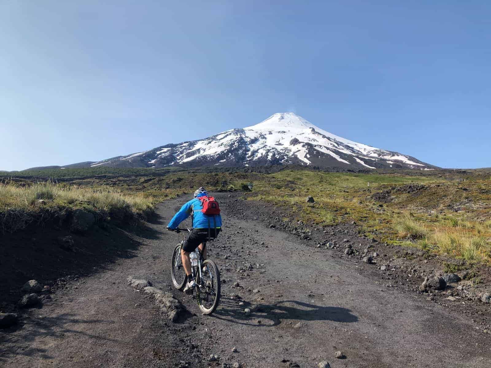 Una persona andando en bicicleta con el Volcán Rukapillan al fondo.