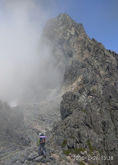 Un hombre parado en la cima de una montaña con una nube al fondo, rodeado de un paisaje sereno y majestuoso.