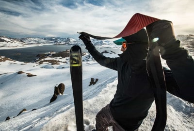 Un hombre sosteniendo sus esquís en la cima de una montaña nevada, con preocupaciones de avalanchas.