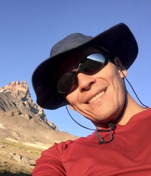 Un hombre con sombrero y gafas de sol frente a una montaña.