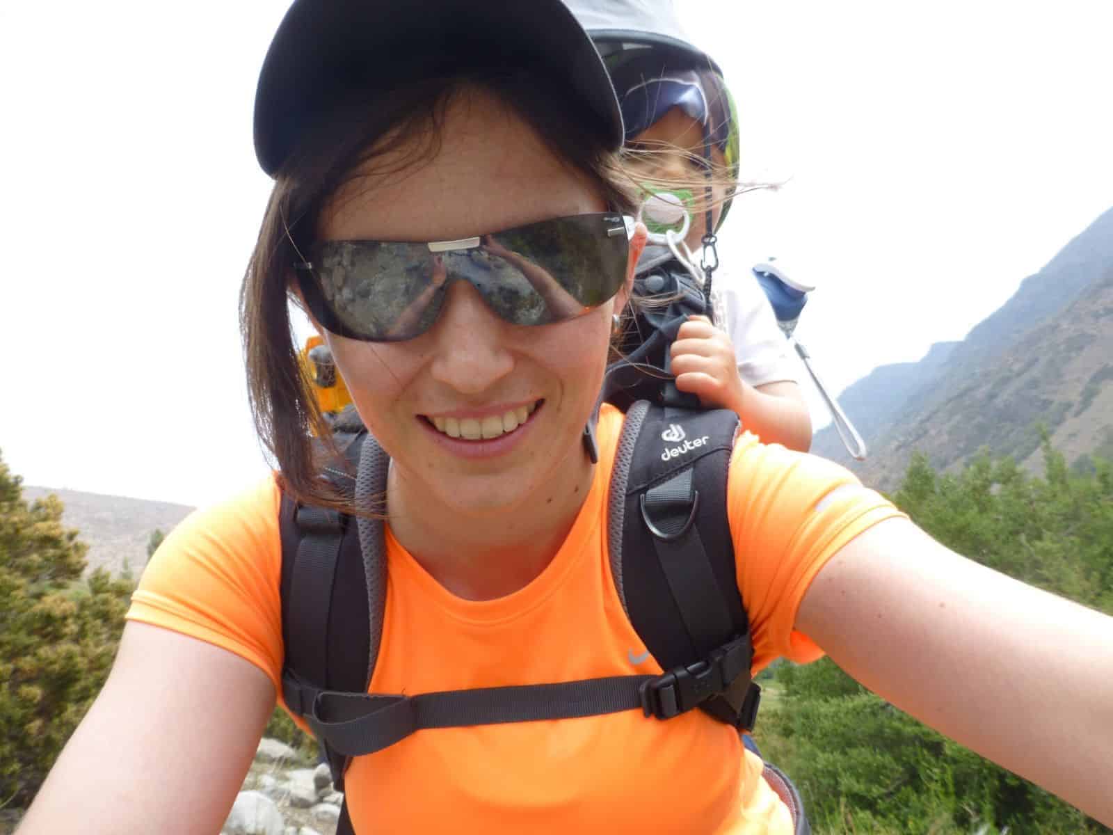 Una mujer, con lentes de sol, se hace un selfie con un niño a la espalda.