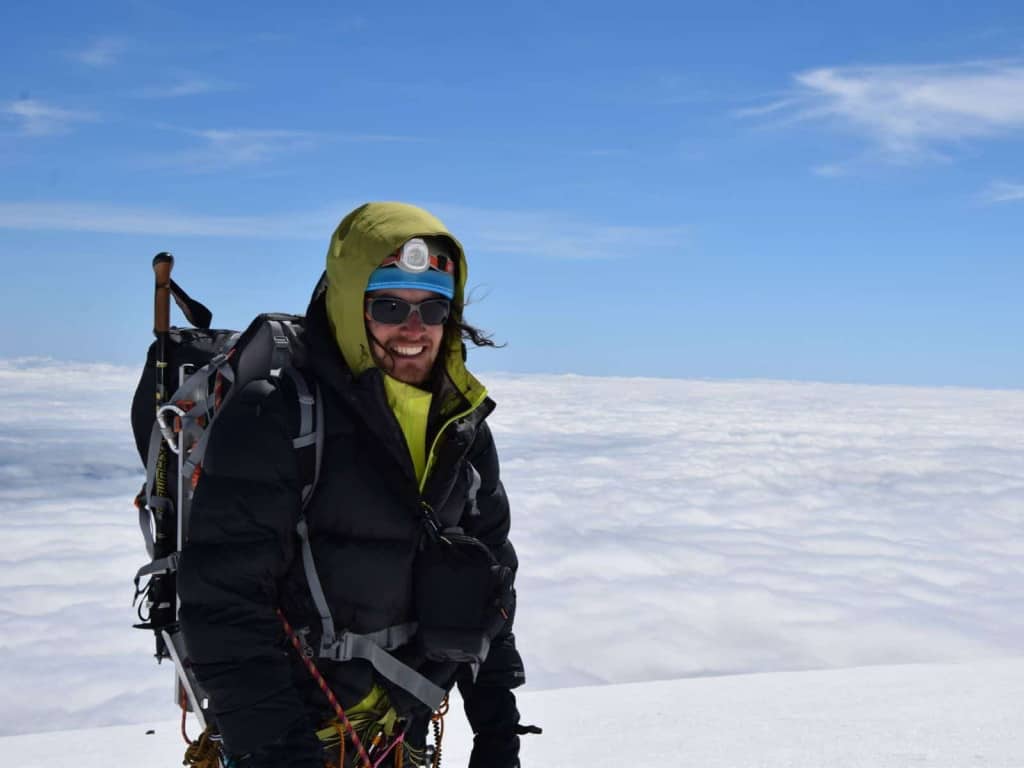 Un hombre con lentes en la cima de una montaña nevada.
