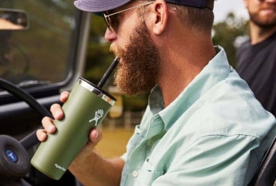 Un hombre conduce un jeep mientras bebe de una taza. La taza contiene una bebida refrescante.