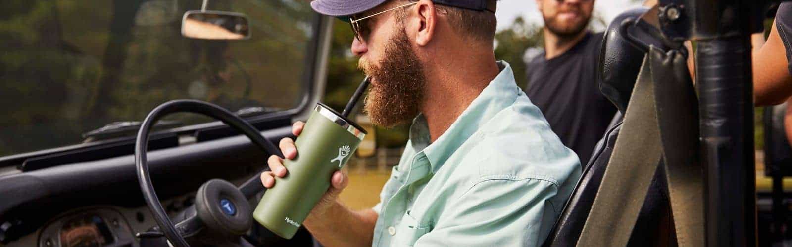 Un hombre conduce un jeep mientras bebe de una taza. La taza contiene una bebida refrescante.