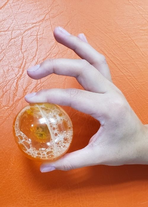 La mano de una persona sosteniendo una bola naranja sobre un fondo naranja, enfatizando la importancia de la kinesiología en la prevención de lesiones.