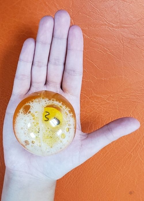 La mano de una persona sosteniendo una bola naranja con burbujas, estudiando su kinesiología para detectar lesiones relacionadas con la escalada.