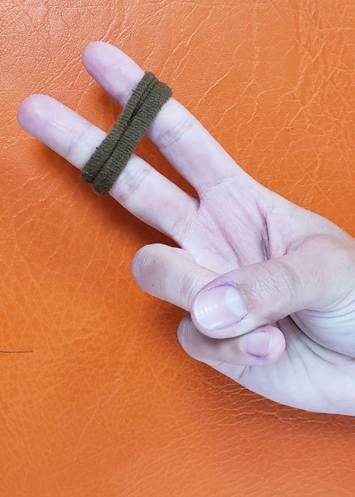 La mano de una persona sosteniendo un par de lazos verdes para actividades de kinesiología y prevención de lesiones.