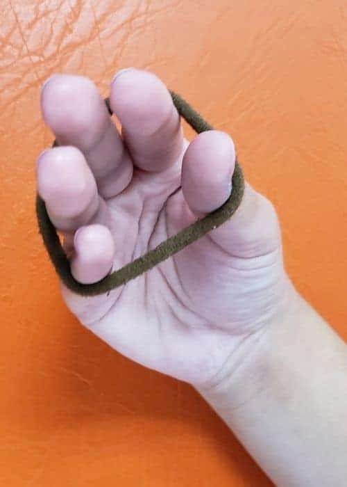 La mano de una persona sosteniendo una banda elástica durante un ejercicio de kinesiología y prevención de lesiones en la escalada.