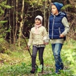 Dos niños paseando por una zona boscosa, rodeados de celulosas.