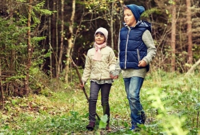 Dos niños paseando por una zona boscosa, rodeados de celulosas.