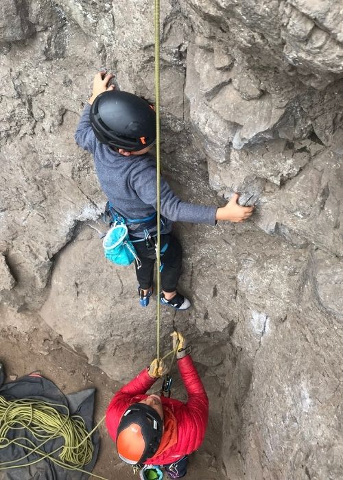 Un niño aventurero está escalando una imponente roca al aire libre, firmemente atado por una cuerda.