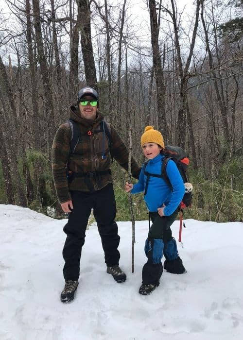 Un hombre y un niño se aventuran valientemente en la naturaleza nevada, dejando atrás su zona de confort para vivir una emocionante aventura familiar al aire libre.