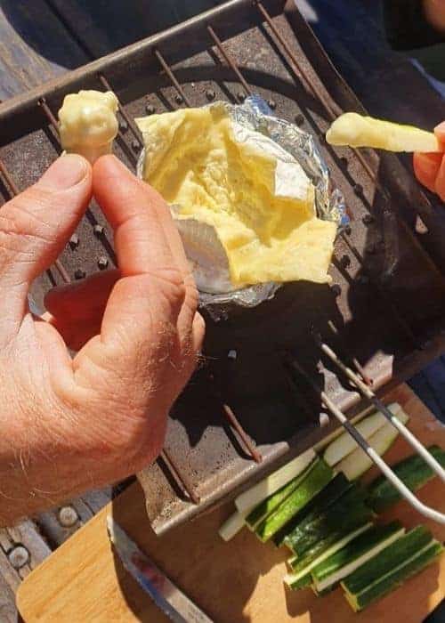 Una parrilla al aire libre con una persona sosteniendo un trozo de queso.