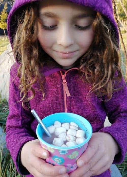 Una niña sosteniendo un plato de malvaviscos al aire libre con su familia.