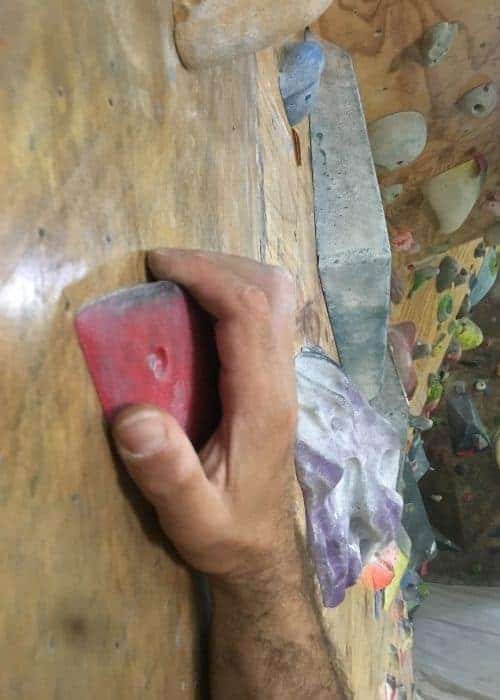 Una mano practica técnicas de búlder en un muro de escalada.