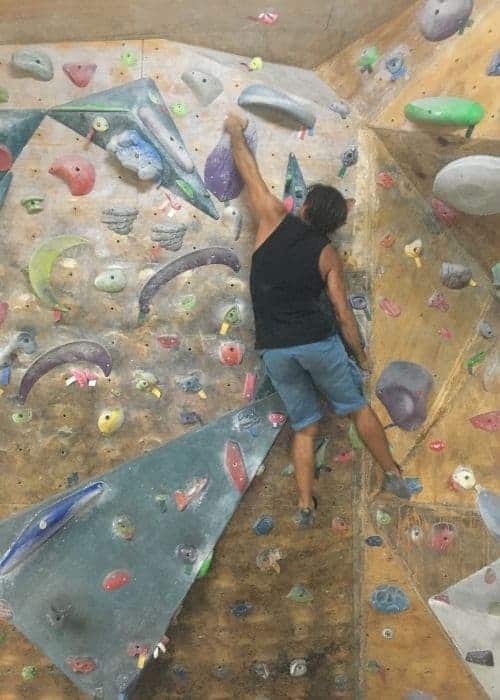 Un hombre trepando por una pared de roca en un gimnasio, practicando técnicas y ejercicios de escalada.