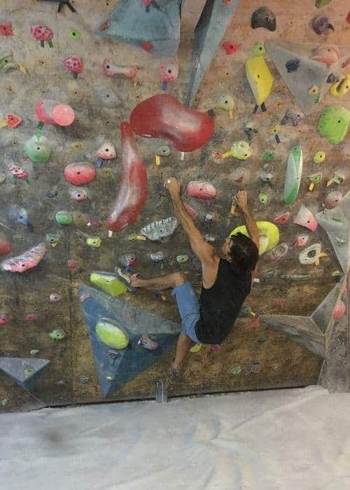 Un hombre practicando técnicas de boulder en una pared de roca en un gimnasio.