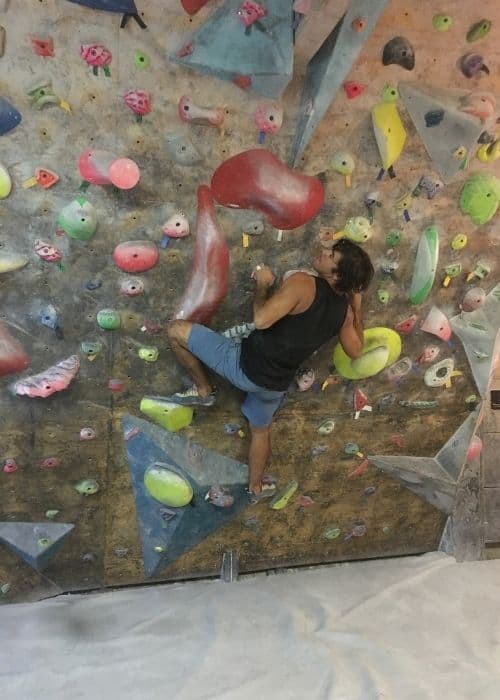 Un hombre practicando técnicas de boulder en un muro de escalada en un gimnasio.