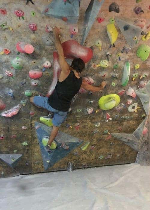 Un hombre realizando ejercicios de boulder mientras trepa por una pared en un gimnasio.