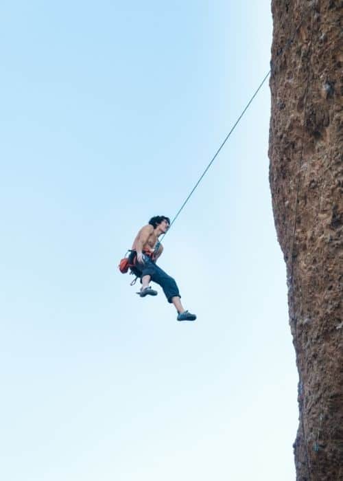 Un hombre practica escalada deportiva mientras asciende por un acantilado con una cuerda.