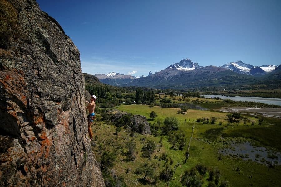 Un hombre practica escalada deportiva en la ladera de una montaña con montañas al fondo.