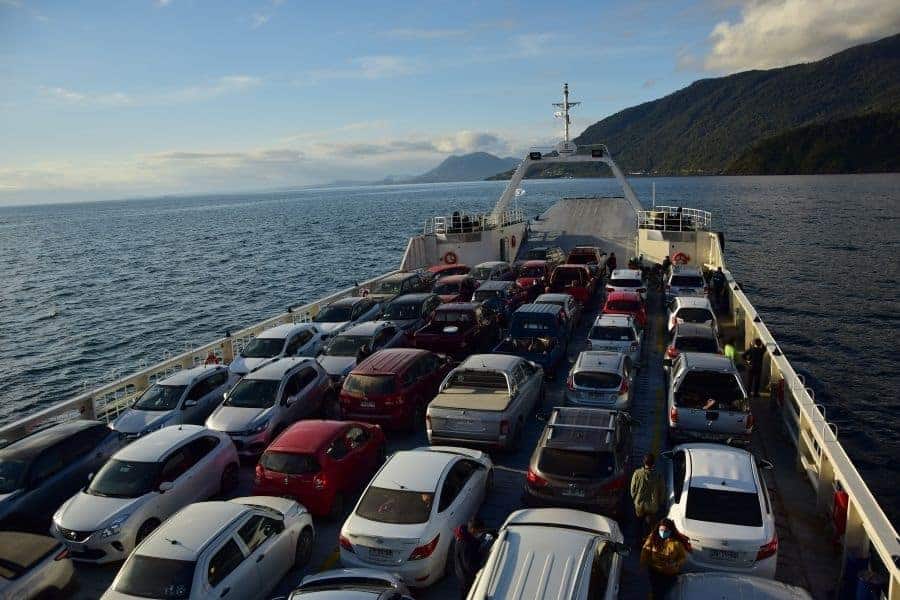 Muchos autos están estacionados en la parte trasera de un ferry, con el impresionante telón de fondo de las montañas de los Andes y el Volcán Yates.