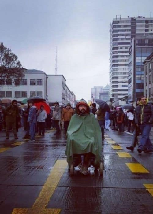 Un hombre inclusivo en silla de ruedas navegando por una calle lluviosa.