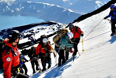 Un grupo de personas en una expedición inclusiva, liderados por su guía, subiendo una montaña nevada.