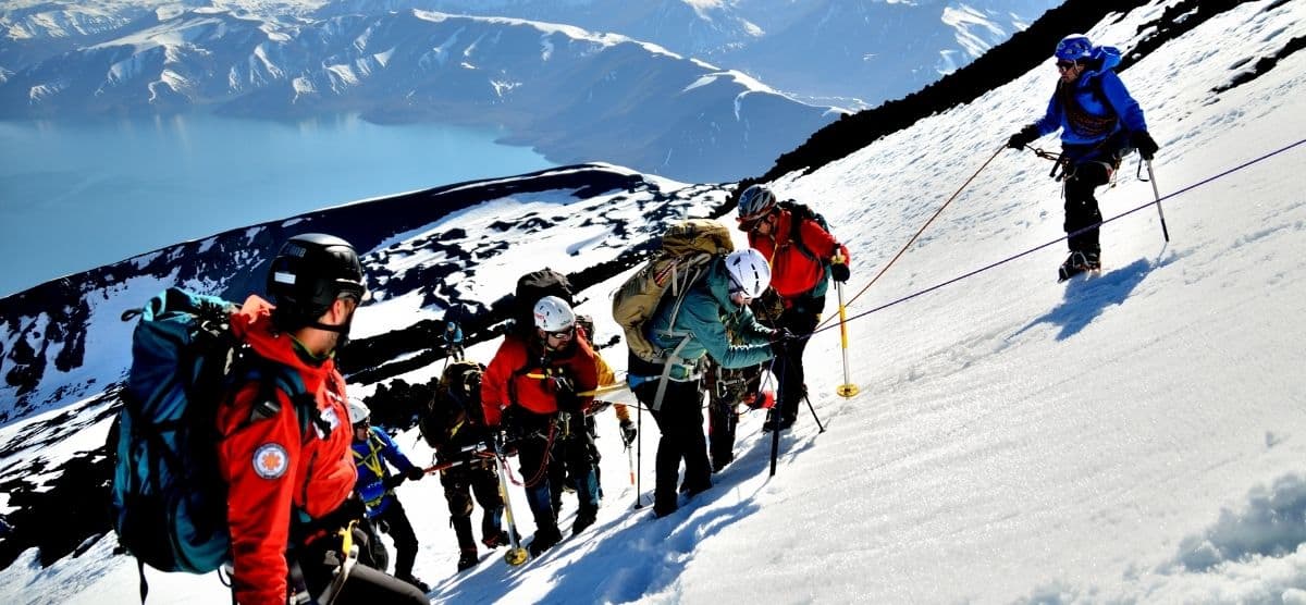 Un grupo de personas en una expedición inclusiva, liderados por su guía, subiendo una montaña nevada.