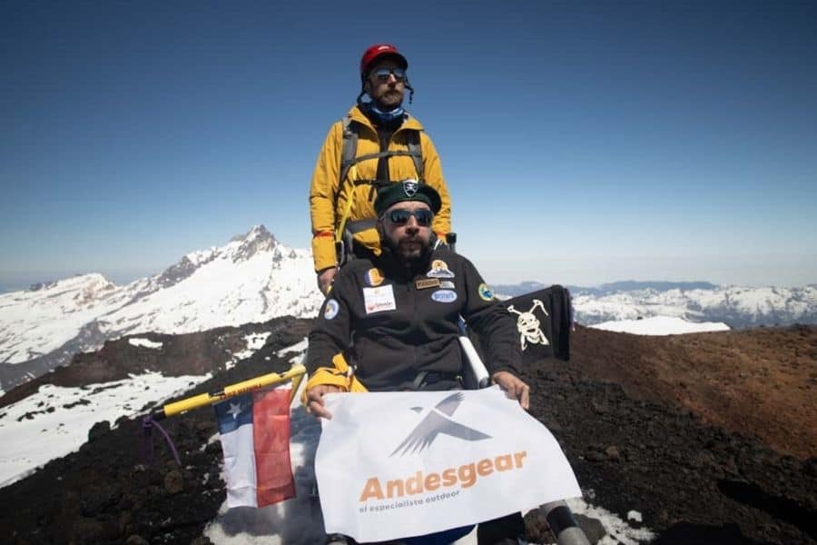 Dos hombres parados en la cima del monte Antuco, sosteniendo un cartel inclusivo.