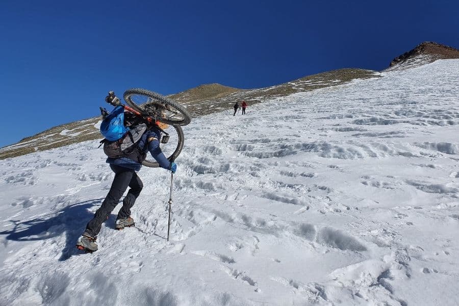 Un hombre llevando una bicicleta por una montaña nevada.