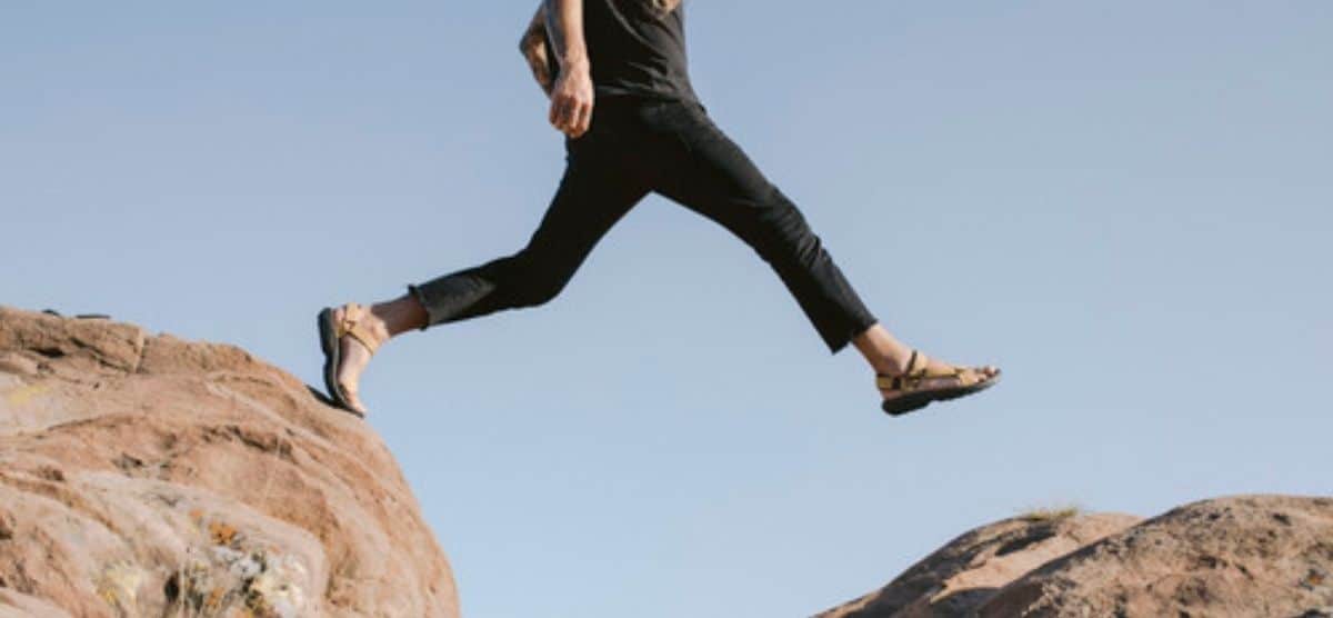 Un aventuero que desafía la gravedad mientras salta con confianza sobre una roca revestida de Teva.