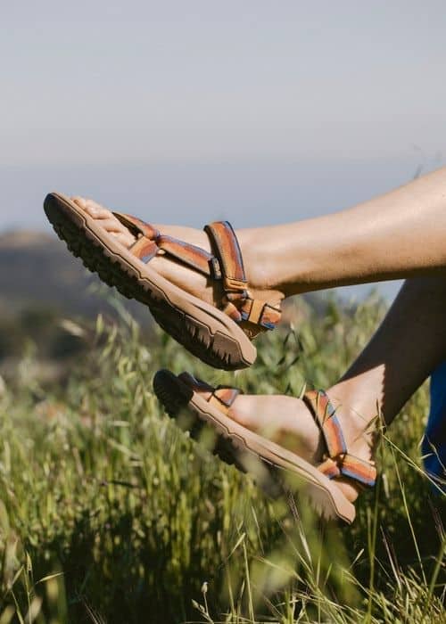 Los pies de una mujer en un campo de hierba con sandalias aventueros.