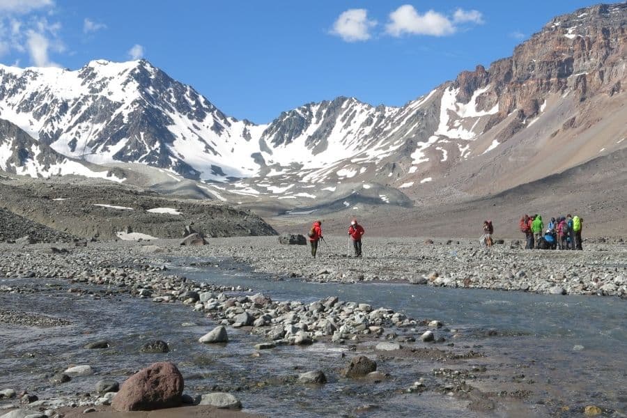 Un grupo de personas de pie cerca de un río con la montaña Marmolejo al fondo.
