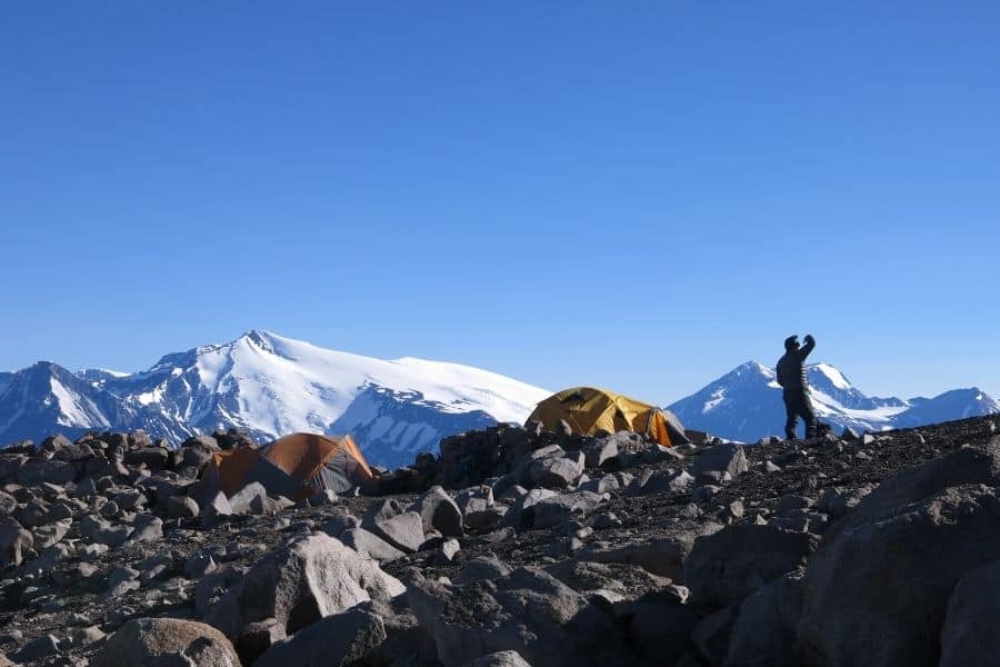 Un hombre parado en la cima de la montaña Marmolejo de seis mil pies de altura con tiendas de campaña al fondo.