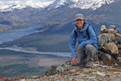 Un explorador sentado en la cima del Monte O'Higgins en la Patagonia, con las montañas circundantes.