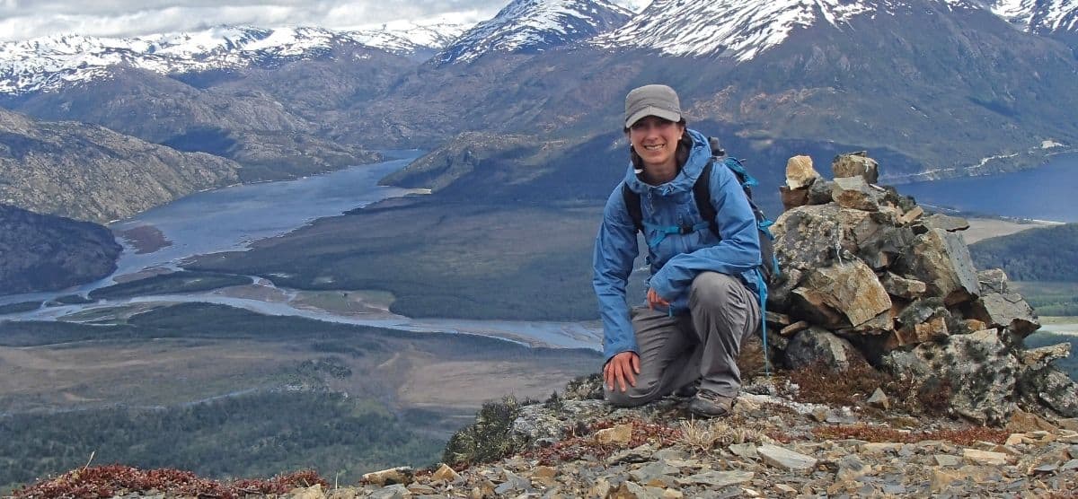 Un explorador sentado en la cima del Monte O'Higgins en la Patagonia, con las montañas circundantes.