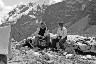 Dos hombres abrazándose amorosamente en la cima de una montaña, de pie junto a una tienda de campaña.